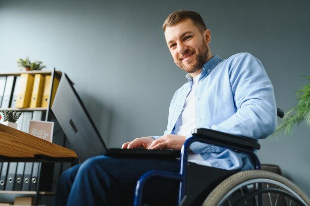 Junger glücklicher Unternehmer im Rollstuhl, der zu Hause am Laptop arbeitet