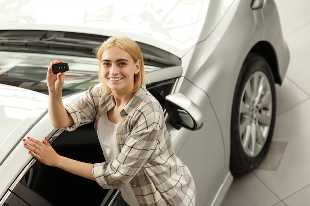 Junger glücklicher weiblicher Fahrer, der Autoschlüssel zu ihrem neuen Automobil halten lächelt.