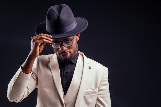 Junger gutaussehender afroamerikanischer melancholischer Junge in weißer Jacke und Brille auf schwarzem Hintergrund im StudioGeheimnis und Trauer