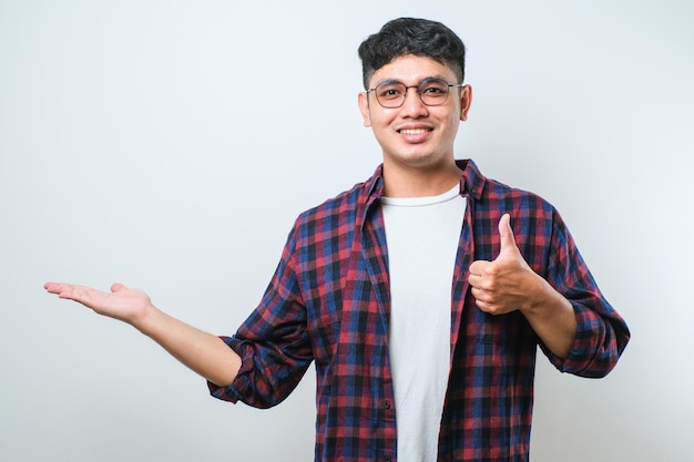 Junger gutaussehender asiatischer mann, der mit dem handfinger zur seite zeigt und in die kamera schaut