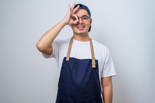 Junger gutaussehender Barista-Mann mit Schürze lächelt und macht mit den Fingern ein ausgezeichnetes Symbol