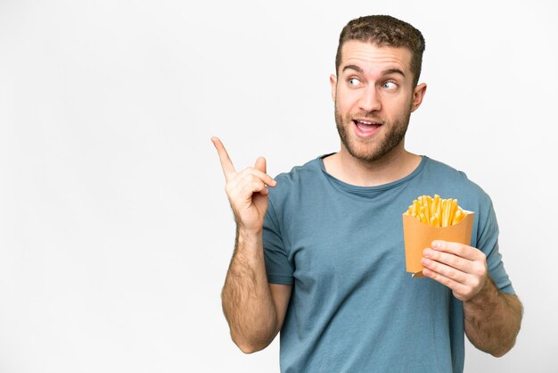 Junger gutaussehender blonder Mann, der gebratene Pommes über isoliertem weißem Hintergrund hält und beabsichtigt, die Lösung zu realisieren, während er einen Finger hochhebt