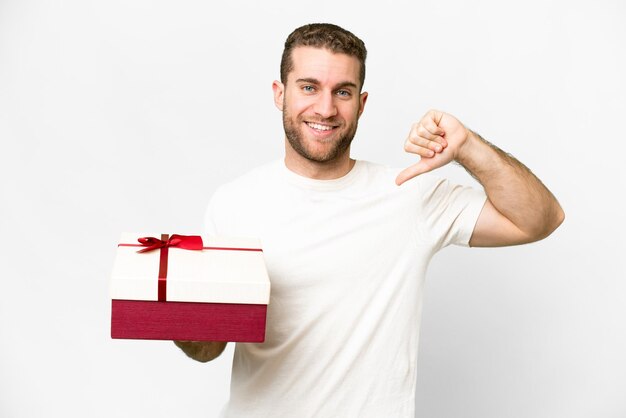 Junger gutaussehender blonder Mann mit einem Geschenk vor isoliertem weißem Hintergrund stolz und selbstzufrieden
