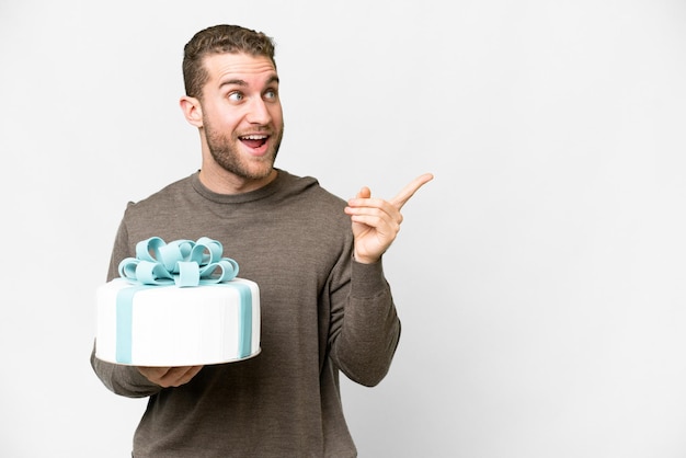 Junger gutaussehender blonder Mann mit einem großen Kuchen vor isoliertem weißem Hintergrund, der beabsichtigt, die Lösung zu realisieren, während er einen Finger hochhebt