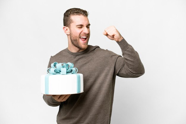 Junger gutaussehender blonder Mann mit einem großen Kuchen vor isoliertem weißem Hintergrund, der einen Sieg feiert