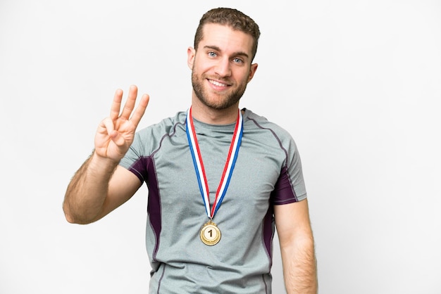 Junger gutaussehender blonder Mann mit Medaillen vor isoliertem weißem Hintergrund glücklich und drei mit den Fingern zählend