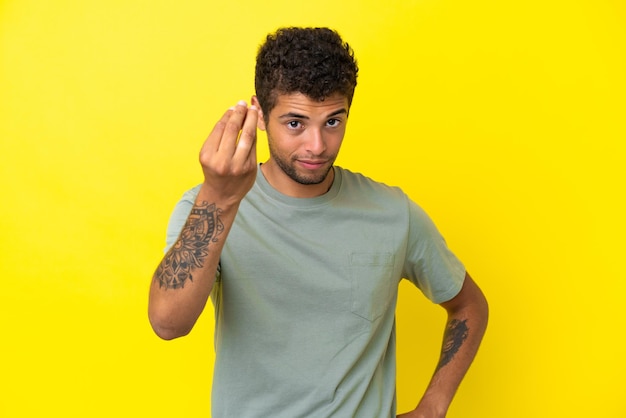 Junger gutaussehender Brasilianer isoliert auf gelbem Hintergrund mit italienischer Geste