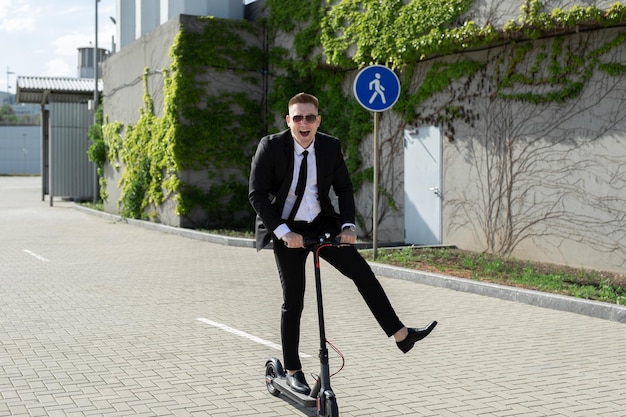 Junger gutaussehender Geschäftsmann im Anzug fährt mit einem Elektroroller durch die Stadt und lacht