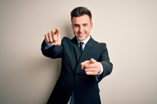 Junger gutaussehender Geschäftsmann in elegantem Anzug und Krawatte vor isoliertem Hintergrund, der mit positiv und fröhlich lächelnden Fingern auf Sie und die Kamera zeigt