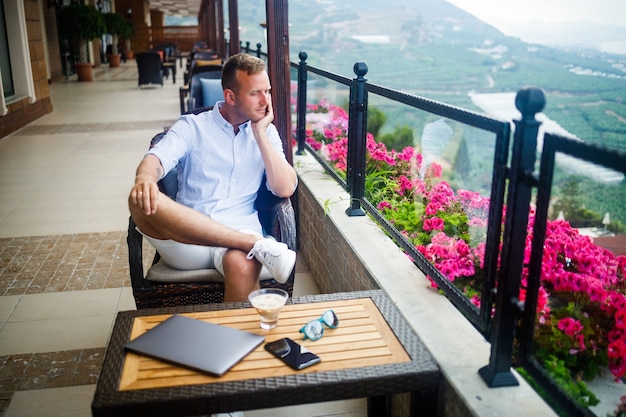 Junger gutaussehender Geschäftsmann in weißem Hemd und Shorts sitzt mit einem Laptop in einem Café am Tisch. Arbeite in Ruhe