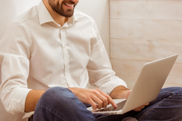 Junger gutaussehender Geschäftsmann in weißem klassischem Hemd und Jeans mit einem Laptop, während er in der Nähe arbeitet