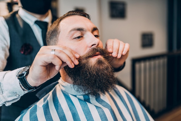 Junger gutaussehender hipster Mann, der einen Friseursalon besucht. Trendiges und stylisches Bartstyling und -schnitt.