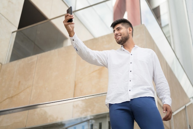 Junger gutaussehender hispanischer Mann, der im Freien ein Selfie mit dem Smartphone macht