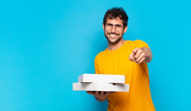 Junger gutaussehender indischer mann, der pizzen zum mitnehmen zeigt oder zeigt und hält