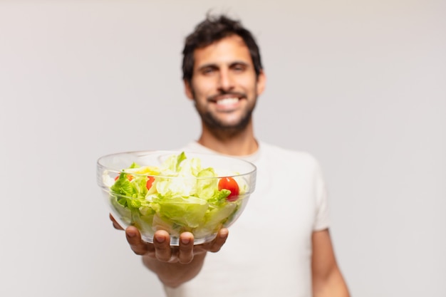 Junger gutaussehender indischer mann mit glücklichem ausdruck, der salat zeigt