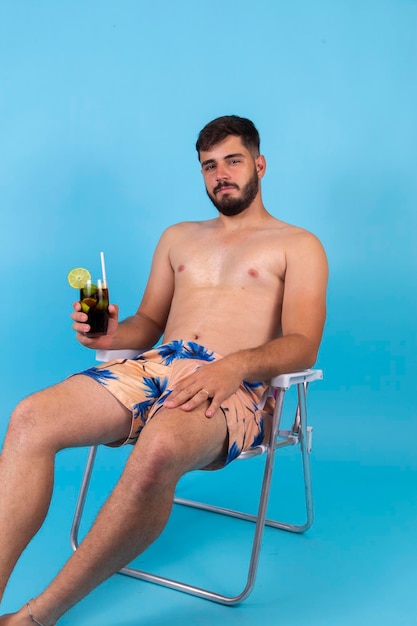 Junger gutaussehender Junge genießt Sommerferien und trinkt kalte Cola Soda Der Mann ist im Urlaub und sitzt auf dem Liegestuhl mit einem Drink