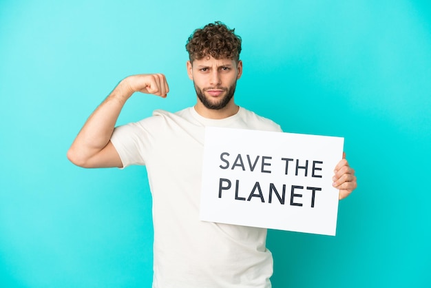 Junger gutaussehender kaukasischer Mann isoliert auf blauem Hintergrund, der ein Plakat mit dem Text "Save the Planet" hält und eine starke Geste macht