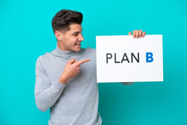 Junger gutaussehender kaukasischer Mann isoliert auf blauem Hintergrund mit einem Plakat mit der Botschaft PLAN B