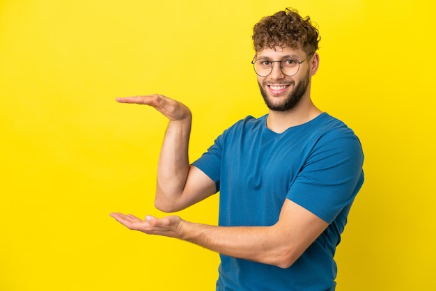 Junger gutaussehender kaukasischer Mann isoliert auf gelbem Hintergrund, der Exemplar hält, um eine Anzeige einzufügen