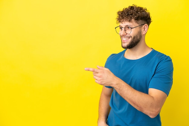 Junger gutaussehender kaukasischer Mann isoliert auf gelbem Hintergrund, der mit dem Finger zur Seite zeigt und ein Produkt präsentiert