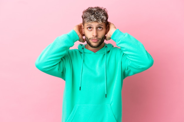 Junger gutaussehender kaukasischer Mann isoliert auf rosa Hintergrund frustriert und bedeckt die Ohren