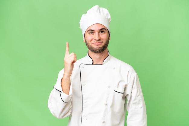 Junger gutaussehender Koch über isoliertem Hintergrund, der mit dem Zeigefinger auf eine großartige Idee zeigt
