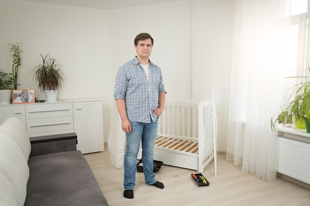 Junger gutaussehender Mann, der am zerlegten Babybett im Schlafzimmer steht