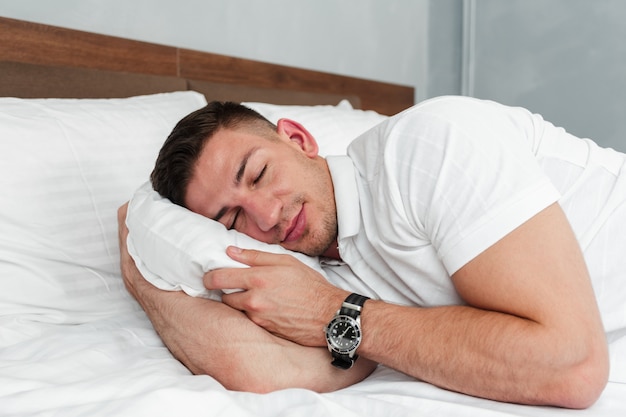 Junger gutaussehender Mann, der auf Bett nach einem harten Tag bei der Arbeit sich entspannt