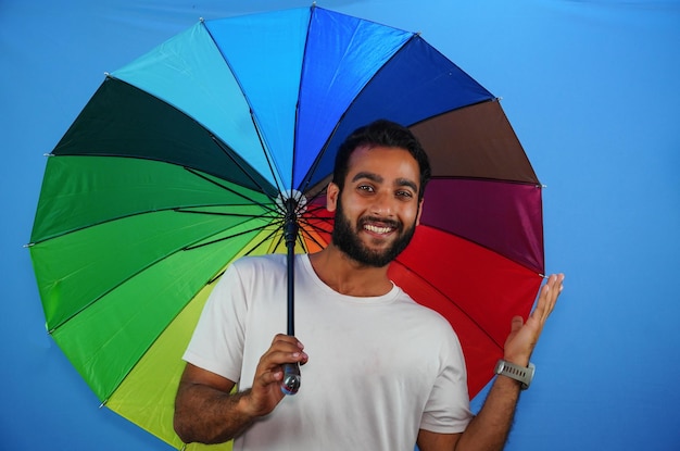 Junger gutaussehender Mann, der bunten Regenschirm hält und erstaunte Ausdrucksangst und aufgeregtes Gesicht gibt