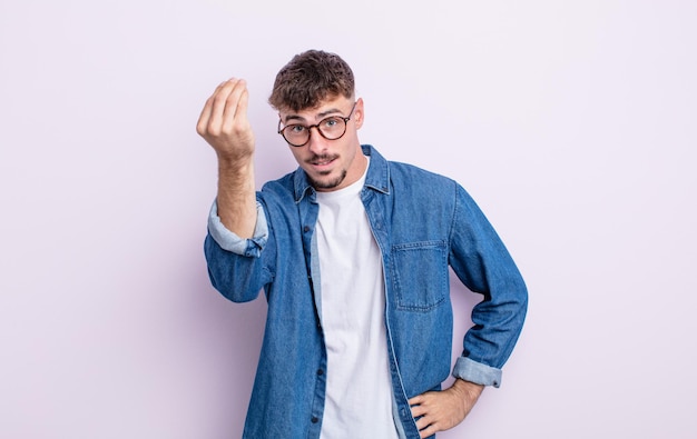 Junger gutaussehender Mann, der eine Capice- oder Geldgeste macht und Ihnen sagt, dass Sie Ihre Schulden bezahlen sollen!