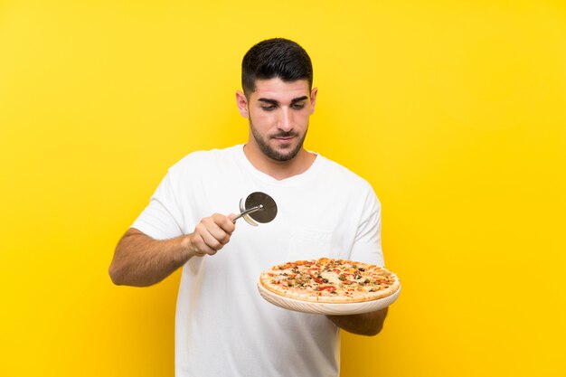 Junger gutaussehender mann, der eine pizza über lokalisierter gelber wand hält