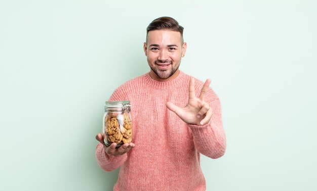 Junger gutaussehender Mann, der freundlich lächelt und aussieht und Nummer drei zeigt. Keksflaschenkonzept