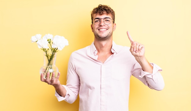 Junger gutaussehender Mann, der freundlich lächelt und aussieht und Nummer eins zeigt. Blumenkonzept