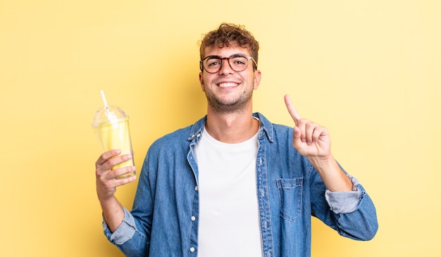 Junger gutaussehender Mann, der freundlich lächelt und aussieht und Nummer eins zeigt. Milchshake-Konzept