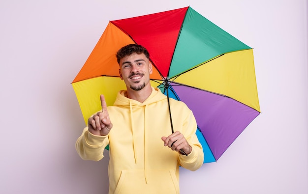 Junger gutaussehender Mann, der freundlich lächelt und aussieht und Nummer eins zeigt. Regenschirmkonzept