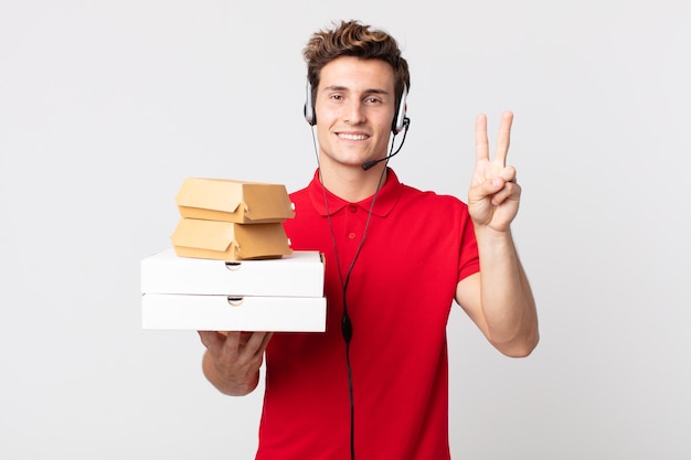 Junger gutaussehender Mann, der freundlich lächelt und aussieht und Nummer zwei zeigt. Take-away-Fast-Food-Konzept