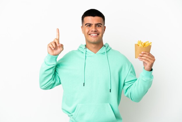 Junger gutaussehender Mann, der gebratene Chips über isoliertem weißem Hintergrund hält und auf eine großartige Idee hinweist