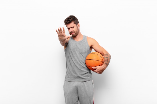 Junger gutaussehender Mann, der Gesicht mit Hand bedeckt und andere Hand nach vorne legt, um Kamera zu stoppen, Fotos ablehnend