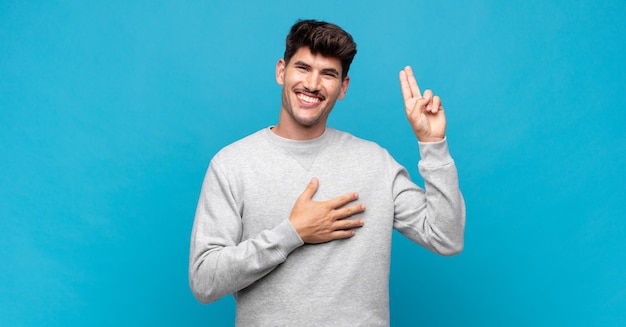 Junger gutaussehender Mann, der glücklich, selbstbewusst und vertrauenswürdig aussieht, lächelt und ein Siegeszeichen zeigt, mit einer positiven Einstellung