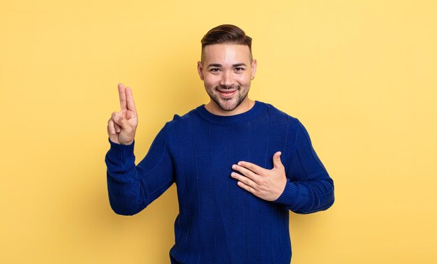 Junger gutaussehender Mann, der glücklich, selbstbewusst und vertrauenswürdig aussieht, lächelt und ein Siegeszeichen zeigt, mit einer positiven Einstellung