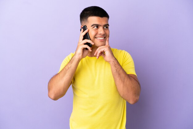 Junger gutaussehender Mann, der Handy über isoliertem lila Hintergrund benutzt und beim Nachschlagen eine Idee denkt