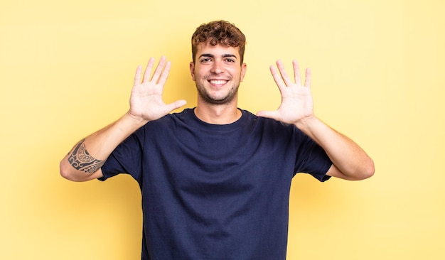 Junger gutaussehender Mann, der lächelt und freundlich aussieht, die Nummer zehn oder zehn mit der Hand nach vorne zeigt und herunterzählt