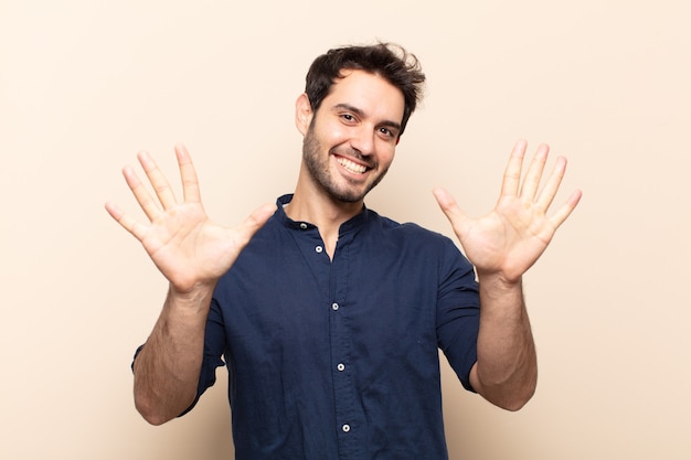 Junger gutaussehender Mann, der lächelt und freundlich aussieht, Nummer zehn oder Zehntel mit der Hand vorwärts zeigend, herunterzählend