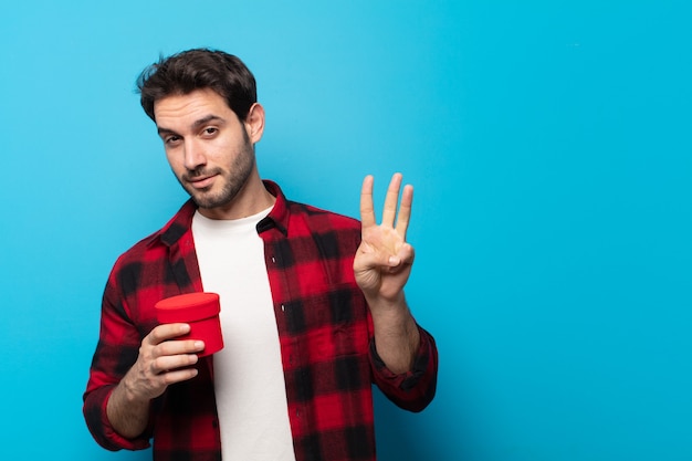 Junger gutaussehender Mann, der lächelt und freundlich schaut, Nummer drei oder dritten mit der Hand vorwärts zeigend, Countdown