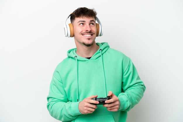 Junger gutaussehender Mann, der mit einem Videospiel-Controller spielt, isoliert auf weißem Hintergrund, denkt an eine Idee, während er nach oben schaut