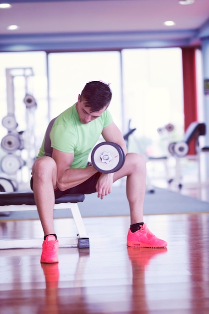 junger gutaussehender mann, der mit hanteln in einem fitnessstudio trainiert