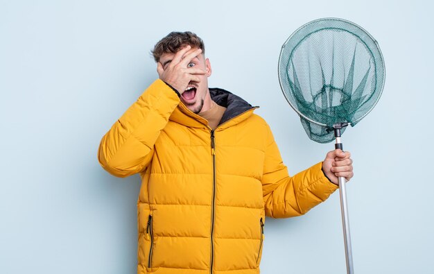 Foto junger gutaussehender mann, der schockiert, verängstigt oder verängstigt aussieht und das gesicht mit dem handfischerkonzept bedeckt