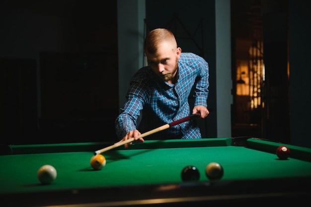 Junger gutaussehender Mann, der sich beim Snooker über den Tisch beugt