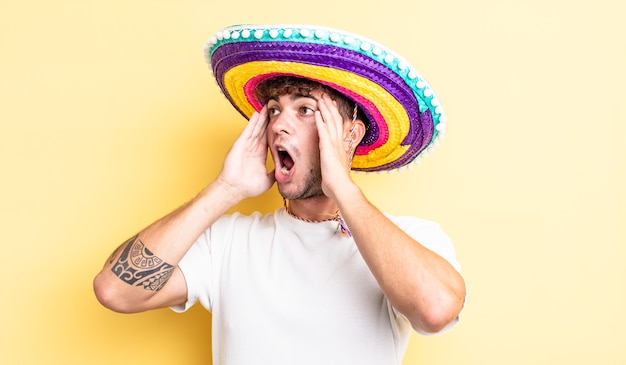 Junger gutaussehender Mann, der sich glücklich, aufgeregt und überrascht fühlt. mexikanisches Hutkonzept
