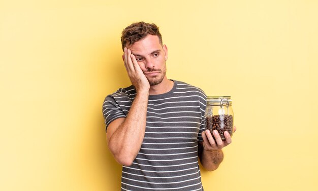 Junger gutaussehender Mann, der sich nach einem ermüdenden Kaffeebohnenkonzept gelangweilt, frustriert und schläfrig fühlt